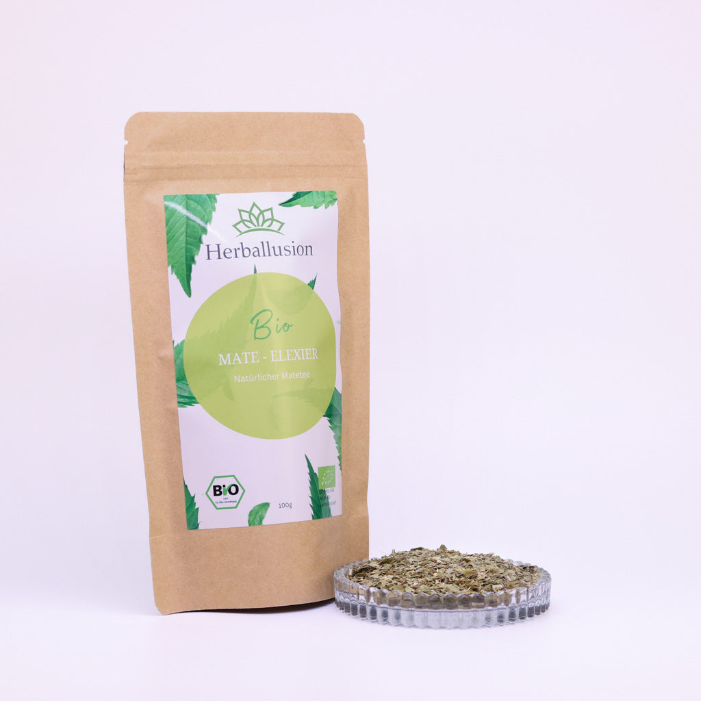 100g-Beutel Bio-Matetee ‚Mate-Elixier‘ mit gelb-grünem Etikett, daneben Glasschale mit losem Tee.