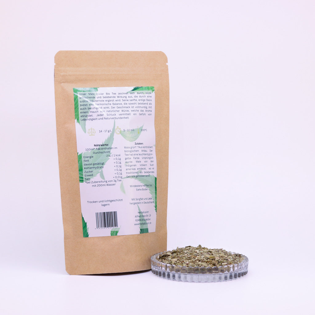 100g-Beutel Bio-Matetee ‚Mate-Elixier‘ mit gelb-grünem Etikett Rückseite, daneben Glasschale mit losem Tee.
