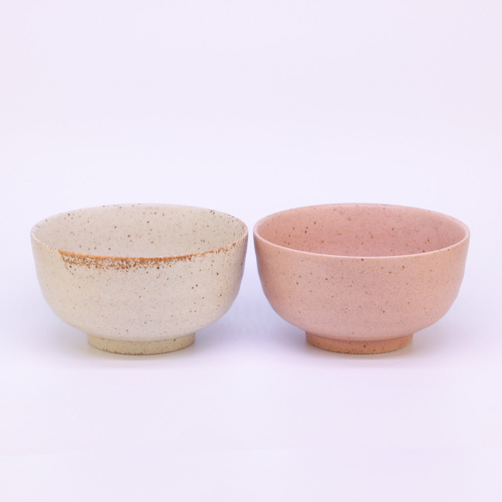Zwei Matcha Schalen: eine in einem creme ton die andere in einem orangeton, stehen nebeneinander auf einem weißem Hintergrund