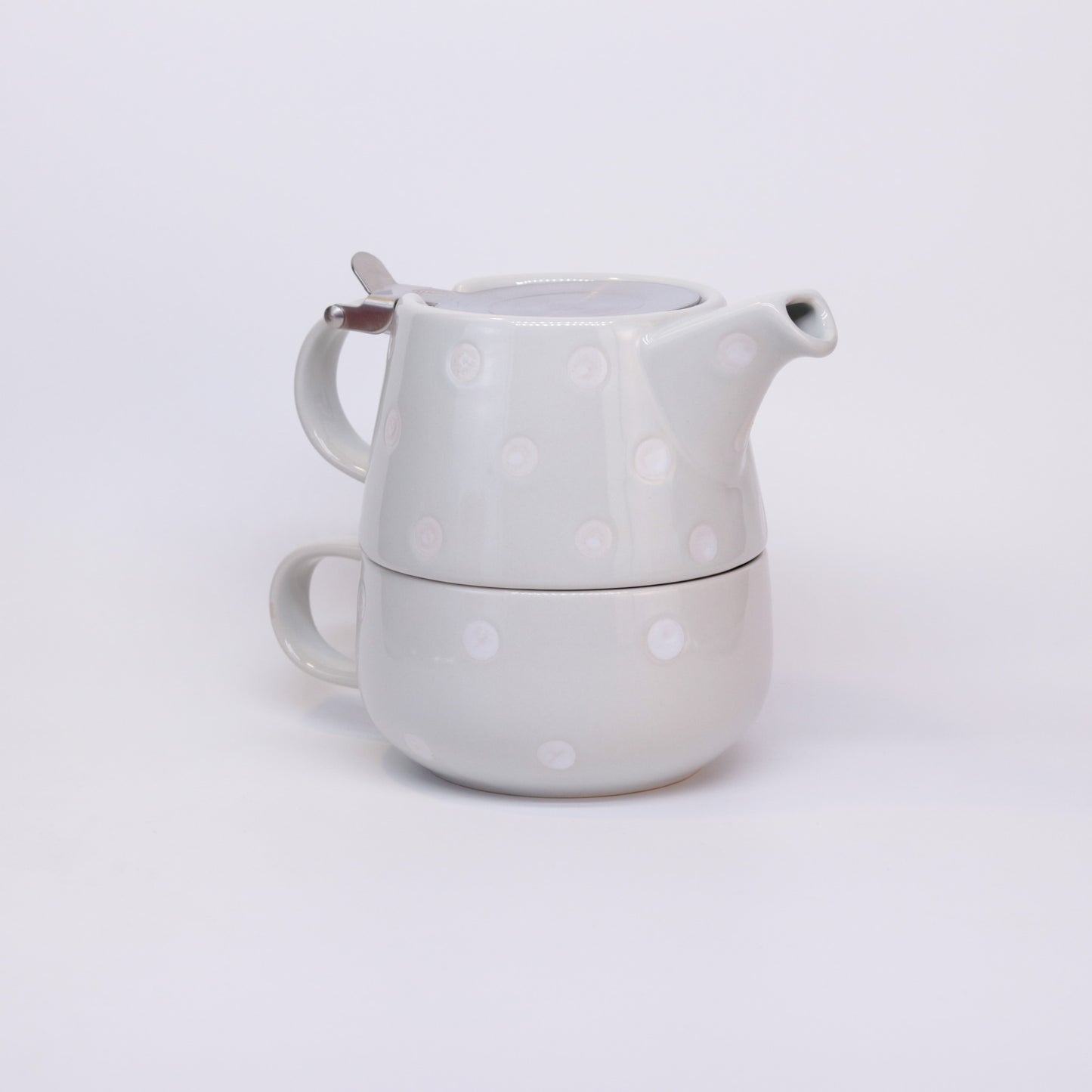 Tasse und Kanne des Tea-for-one Set in grau gepunktet steht als Turm zusammengebaut auf weißem Hintergrund