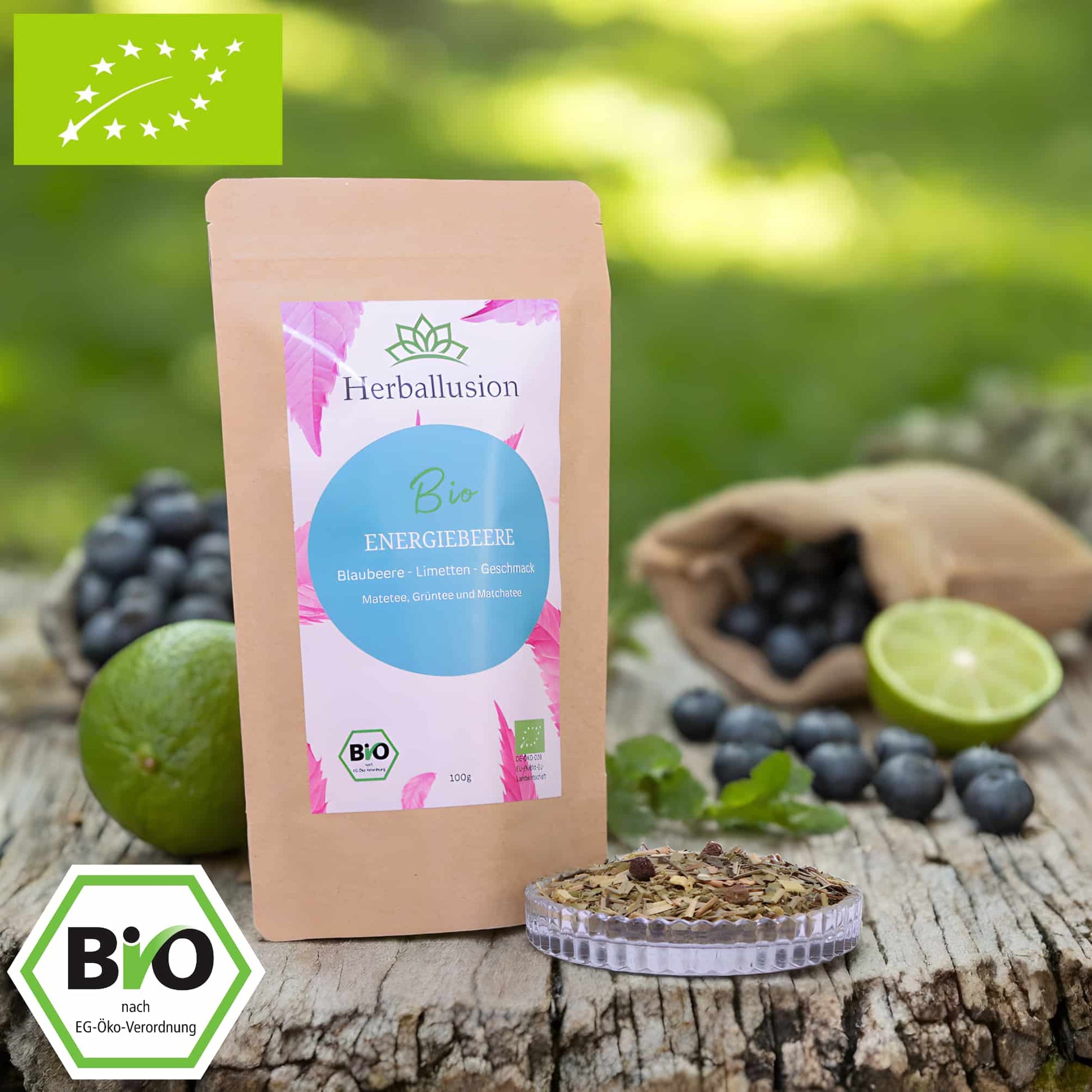 100g-Beutel Bio-Früchtetee ‚Morgenpower‘ mit rosa-blauem Etikett, daneben Glasschale mit losem Tee. Im Hintergrund Zutaten zu sehen sowie Bio und EU Zertifizierung.