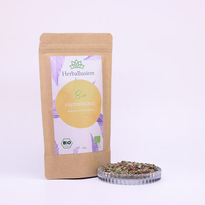 100g-Beutel Bio-Kräutertee ‚Fastenenergie‘ mit orange-lilanem Etikett, daneben Glasschale mit losem Tee.