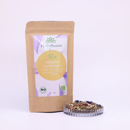 100g-Beutel Bio-Rooibostee ‚Fruchtige Fastenkraft‘ mit orange-lilanem Etikett, daneben Glasschale mit losem Tee.