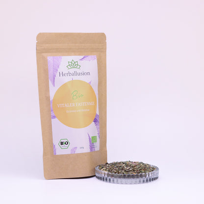100g-Beutel Bio-Grüntee ‚Vitaler Fastenmix‘ mit orange-lilanem Etikett, daneben Glasschale mit losem Tee.