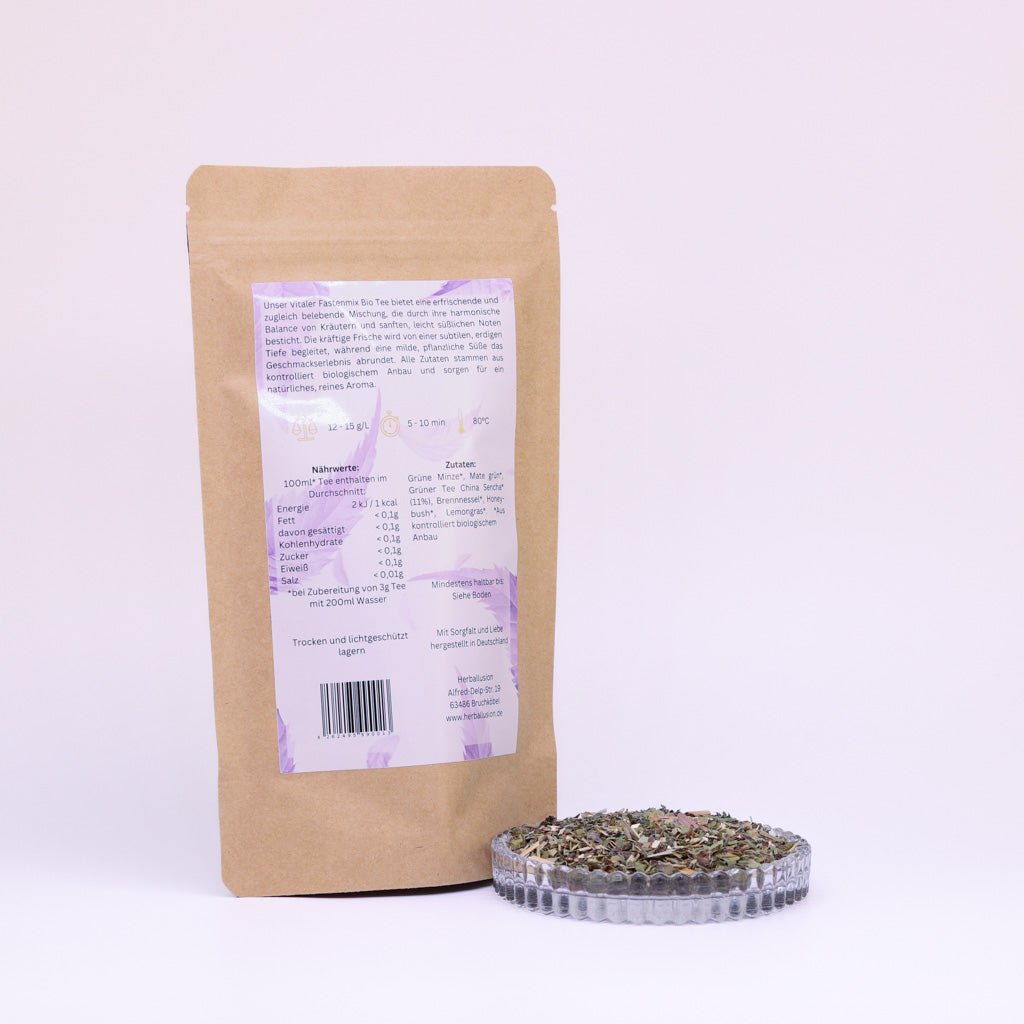 100g-Beutel Bio-Grüntee ‚Vitaler Fastenmix‘ mit orange-lilanem Etikett Rückseite, daneben Glasschale mit losem Tee.