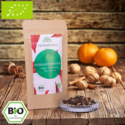 100g-Beutel Bio-Grüntees ‚Weihnachtsmischung‘ mit rot-grünem Etikett, daneben Glasschale mit losem Tee. Im Hintergrund Zutaten zu sehen sowie Bio und EU Zertifizierung.