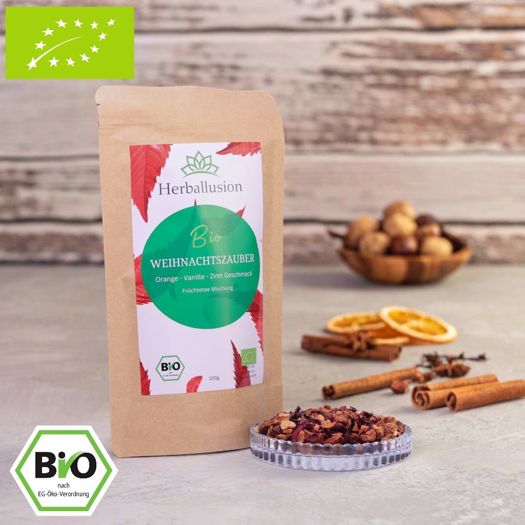 100g-Beutel Bio-Früchtetee ‚Weihnachtszauber‘ mit rot-grünem Etikett, daneben Glasschale mit losem Tee.  Im Hintergrund Zutaten zu sehen sowie Bio und EU Zertifizierung.