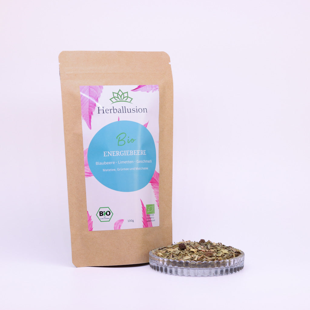 100g-Beutel Bio-Matetee ‚Energiebeere‘ mit rosa-blauem Etikett, daneben Glasschale mit losem Tee.