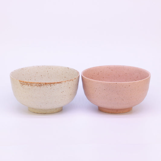 Zwei Matcha Schalen: eine in einem creme ton die andere in einem orangeton, stehen nebeneinander auf einem weißem Hintergrund