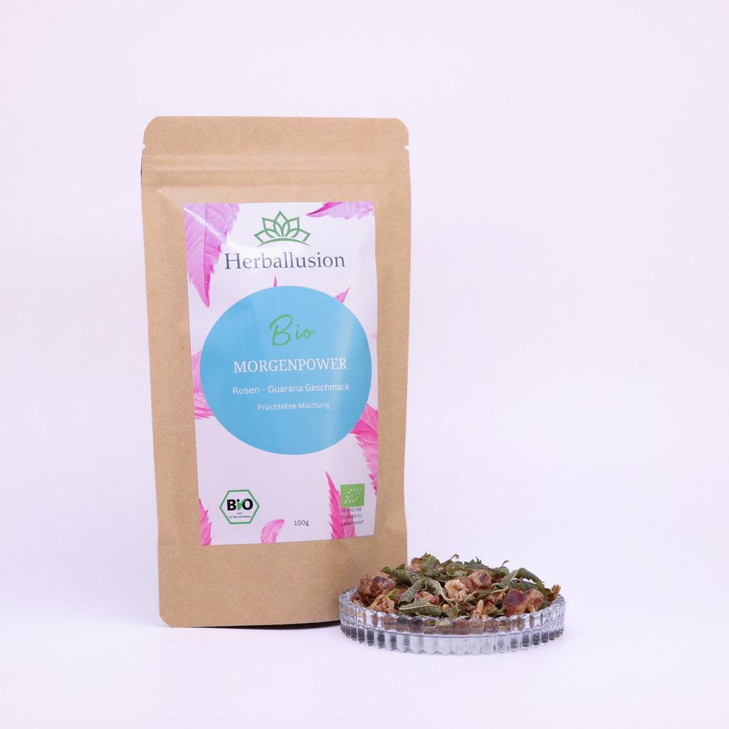100g-Beutel Bio-Früchtetee ‚Morgenpower‘ mit rosa-blauem Etikett, daneben Glasschale mit losem Tee.