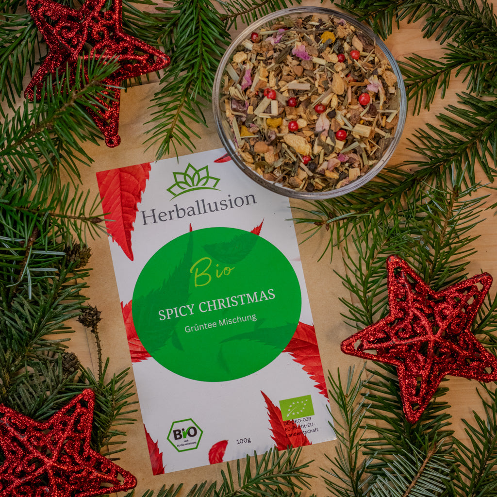 100g Beutel des Bio Grüntees Spicy Christmas auf Holzhintergrund mit weihnachtlicher Deko und Glasschale mit losem Tee