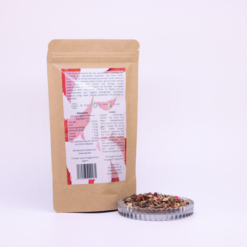100g-Beutel Bio-Grüntees‚Spicy Christmas‘ mit rot-grünem Etikett Rückseite, daneben Glasschale mit losem Tee.