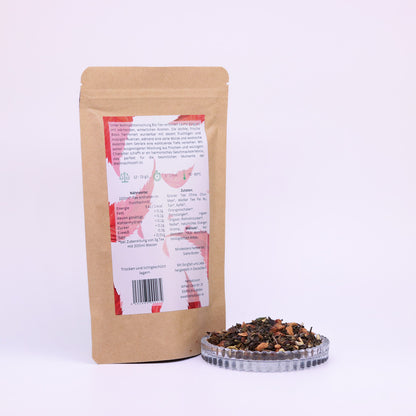 100g-Beutel Bio-Grüntees ‚Weihnachtsmischung‘ mit rot-grünem Etikett Rückseite, daneben Glasschale mit losem Tee.