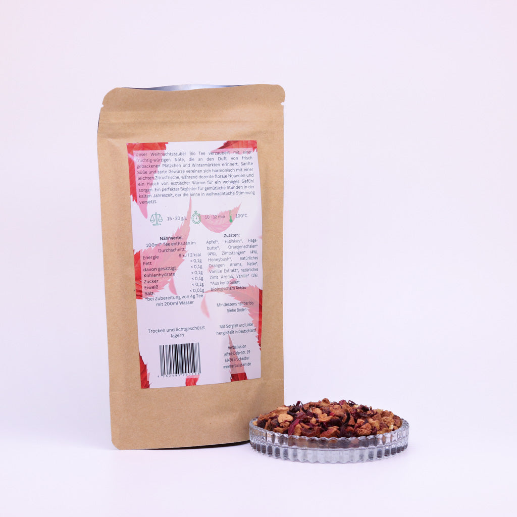 100g-Beutel Bio-Früchtetee ‚Weihnachtszauber‘ mit rot-grünem Etikett Rückseite, daneben Glasschale mit losem Tee.