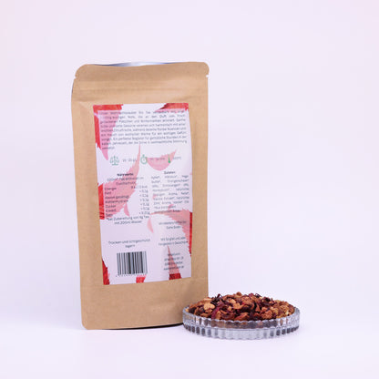 100g-Beutel Bio-Früchtetee ‚Weihnachtszauber‘ mit rot-grünem Etikett Rückseite, daneben Glasschale mit losem Tee.