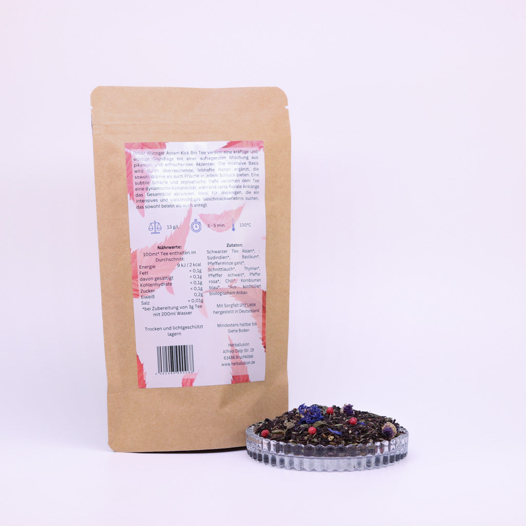 100g-Beutel Bio-Schwarztee ‚Würziger Assam Kick‘ mit rot-blauem Etikett Rückseite, daneben Glasschale mit losem Tee.