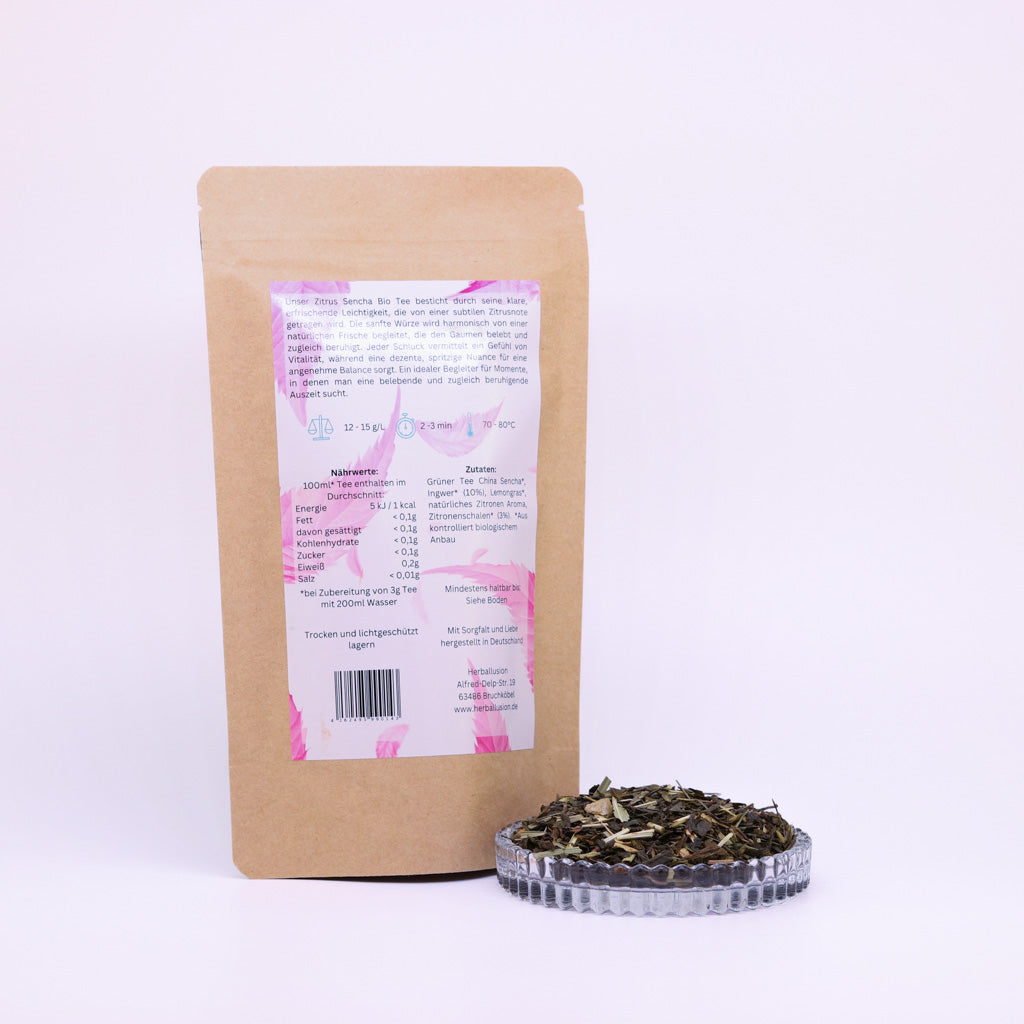100g-Beutel Bio-Grüntee ‚Zitrus Sencha‘ mit rosa-blauem Etikett Rückseite, daneben Glasschale mit losem Tee.